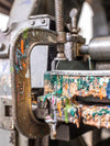 Close-up of a clamp with colorful ink splashes on a blurred industrial background
